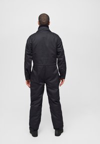 Black padded jumpsuit with a high collar, long sleeves, and elastic cuffs. Features a cinched waist and zippered pockets on the sides.