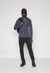 Felpa con zip blu navy dal design aderente, abbinata a pantaloni neri e robusti stivali neri. Dotata di cappuccio e coulisse regolabili.