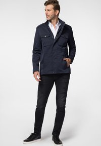 Granatowa kurtka z dwoma kieszeniami na piersi, zapinana na zamek, z guzikami jako akcentami. Połączona z czarnymi znoszonymi dżinsami i czarnymi sneakersami.