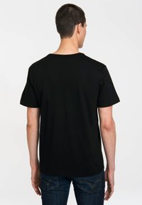 Black cotton t-shirt with short sleeves, round neckline, and a smooth texture, shown from the back, paired with dark denim jeans.