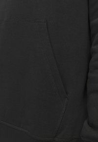 Schwarzer Hoodie mit Kängurutasche, glatter Textur und gerippten Bündchen. Genaue Nähte entlang der Nähte verleihen strukturelles Interesse.
