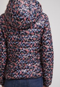 Giacca imbottita floreale blu navy con cappuccio. Presenta una texture lucida e trapuntata, decorata con fiori rosa e blu su uno sfondo scuro.