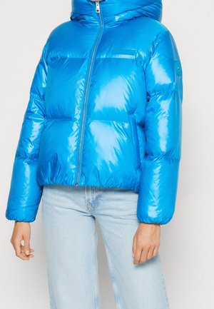 Doudoune bleue brillante avec capuche, fermeture éclair et manches longues portée avec un jean bleu clair sur une personne.
