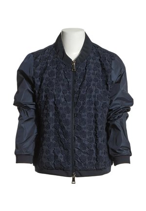 Chaqueta bomber azul marino con frente de encaje floral, mangas lisas, cuello y puños acanalados, y cierre frontal con cremallera sobre un maniquí sin cabeza.