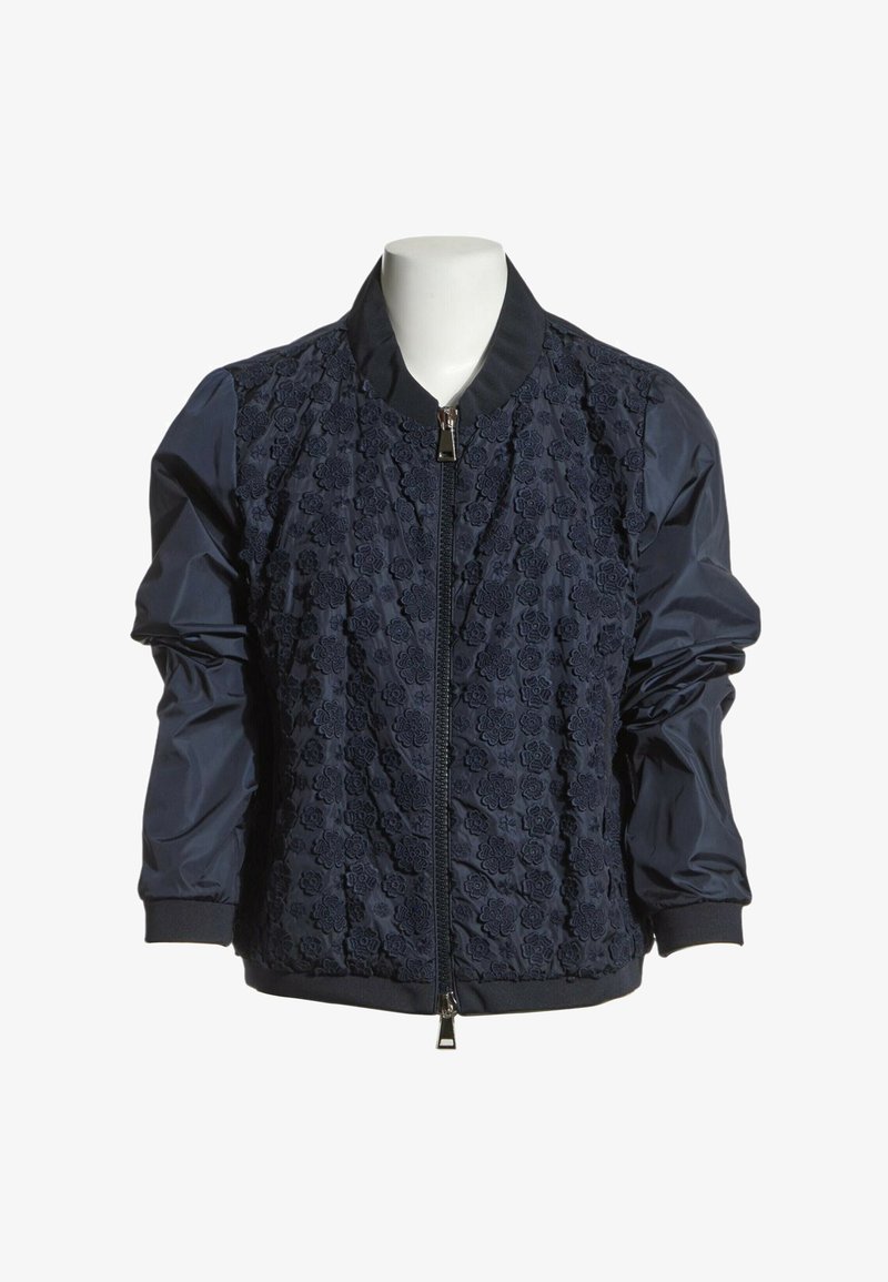 Blouson bomber bleu marine avec devant en dentelle florale, manches unies, col et poignets côtelés, fermeture éclair frontale sur un mannequin sans tête.