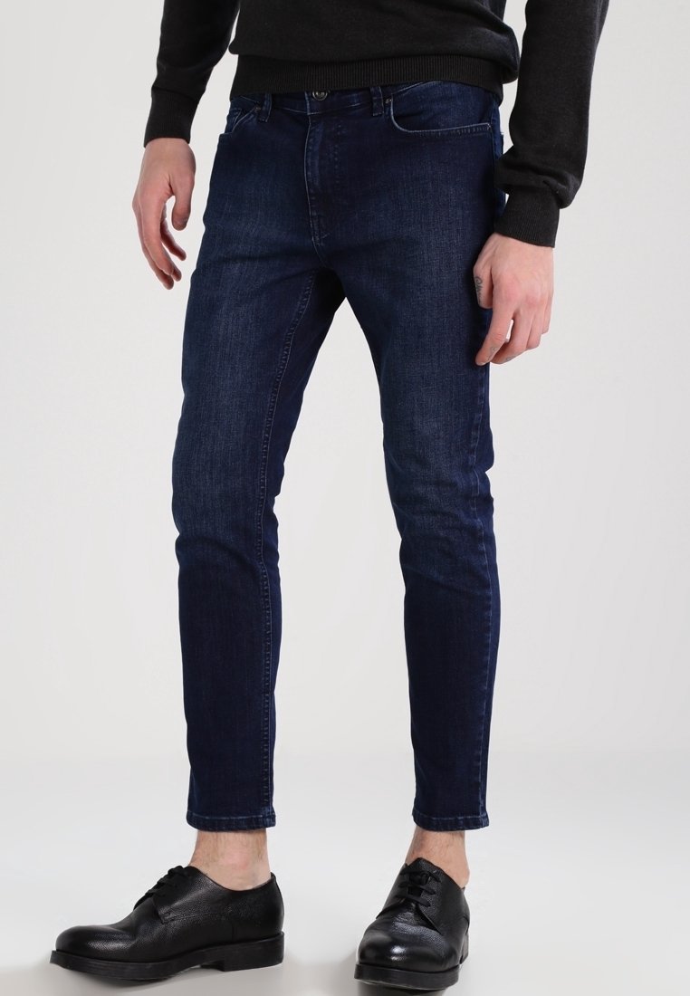 Dark blue denim jeans, slim fit, mid-rise design with a smooth texture and minimal stitching. Worn with black leather shoes.