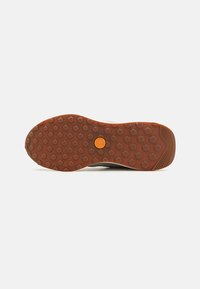 Shoe outsole featuring a textured brown rubber with circular patterns, a logo in the center, and a slightly elevated heel edge for traction.