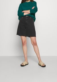 Gonna di jeans nera con orlo sfrangiato, abbinata a una camicia a maniche lunghe turchese e sandali beige con suola nera.