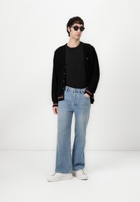 Čierny cardigan s červenými a bielymi pruhmi, čierne tričko, svetlomodré široké džínsy a biele tenisky. Okrúhle čierne slnečné okuliare dopĺňajú outfit.