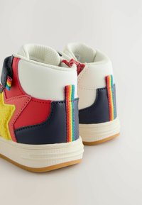 Augstāka stila sneakers ar daudzkrāsainām sintētiskām paneļiem, dzeltenu pūkainu zvaigznes detaļu un varavīksnes svītru akcents uz papēža.