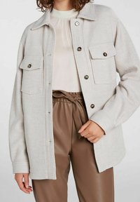 Jasnoszara polarowa kurtka z guzikami z przodu, dwoma kieszeniami na piersi oraz kołnierzykiem. Posiada luźny krój i teksturowany materiał.