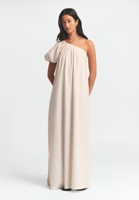 Ühe õlavarrega maksimekk valges beežis kangas, millel on kogutud kaelus, lõtv lõige ja voolav, põrandani ulatuv disain.