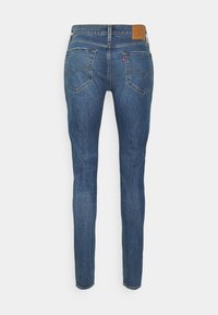 Skinny-fit blue denim jeans with a brown leather waistband label, five pockets, and a faded texture at the legs.