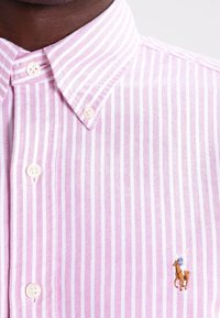 Jasnoróżowa koszula w paski z bawełny z kołnierzykiem zapinanym na guziki. Posiada białe i ciemnoróżowe paski oraz małe haftowane logo konika.