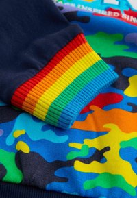 Felpa multicolore con polsini a coste blu navy decorati con strisce arcobaleno. Il corpo presenta un vivace motivo camouflage in blu, verde, arancione e giallo.