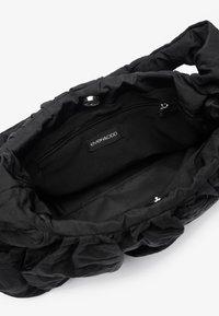 Svart stoffveske med en myk, teksturert overflate. Innvendig har den en glidelåslomme og et merke. Rynket design rundt åpningen.