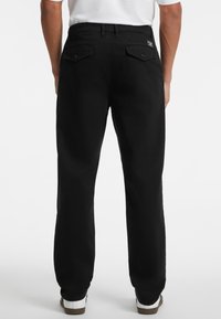 Schwarze Hose mit geradem Schnitt, aus robuster Stoffqualität. Verfügt über Gesäßtaschen mit Knopfverschlüssen und einem Etikett am Bund.