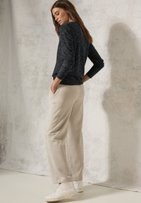 Dunkelgrauer, strukturierten Sweatshirt, beigefarbene, weitgeschnittene Hose und weiße Sneakers. Das Model steht mit den Händen in den Taschen, von hinten betrachtet.