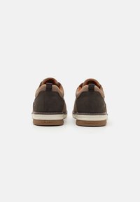 Chaussures en suède marron avec une tige en maille, des accents orange et une semelle en caoutchouc blanche. Comprend une languette à l'arrière et un logo de marque sur la semelle.