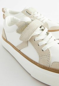 Baskets blanches en cuir avec des accents en daim beige, fermeture à lacets et bande Velcro, dotées d'une semelle en caoutchouc texturé et de détails cousus.