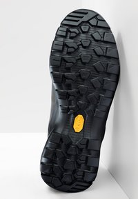 Semelle de chaussure en caoutchouc noir avec un motif de texture antidérapant, featuring des accents hexagonaux et triangulaires. Logo Vibram affiché en jaune.