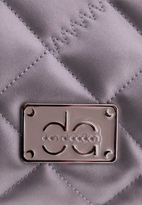 Cuero sintético gris acolchado con una placa de logo plateada que muestra "don algodón." Patrones de costura notables añaden textura a la superficie.