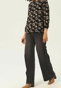 Svart blommig topp med trekvartsärmar, kombinerad med vida mörkdenimjeans och beige högklackade skor. Minimalistisk estetik.