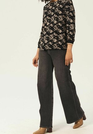 Schwarzes Floral-Top mit Dreiviertelärmeln, kombiniert mit weiten, dunklen Denim-Jeans und hellbraunen High-Heels. Minimalistisches Ästhetik.