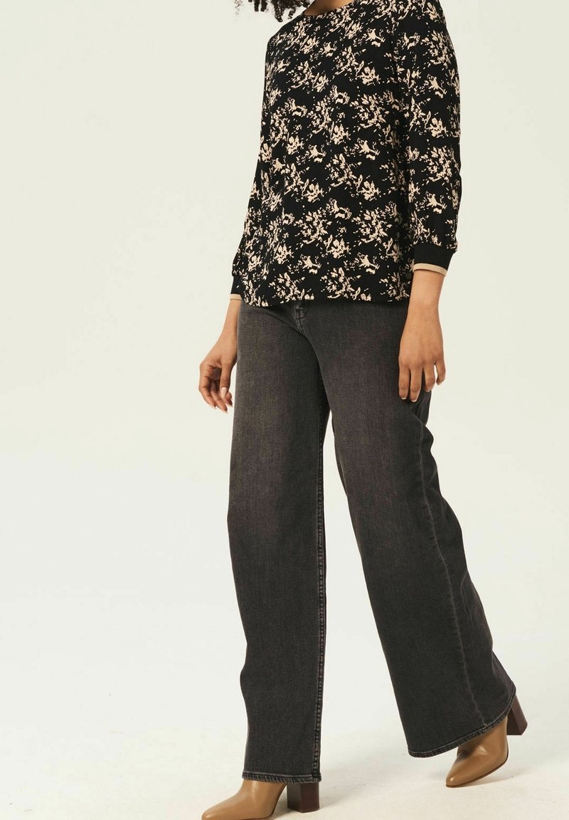 Svart blommig topp med trekvartsärmar, kombinerad med vida mörkdenimjeans och beige högklackade skor. Minimalistisk estetik.