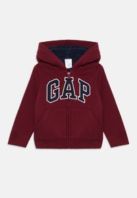 Felpa con zip color bordeaux, con interno in pile, tasche frontali e un grande logo GAP in blu navy sul petto. Presenta polsini e orlo a costine.