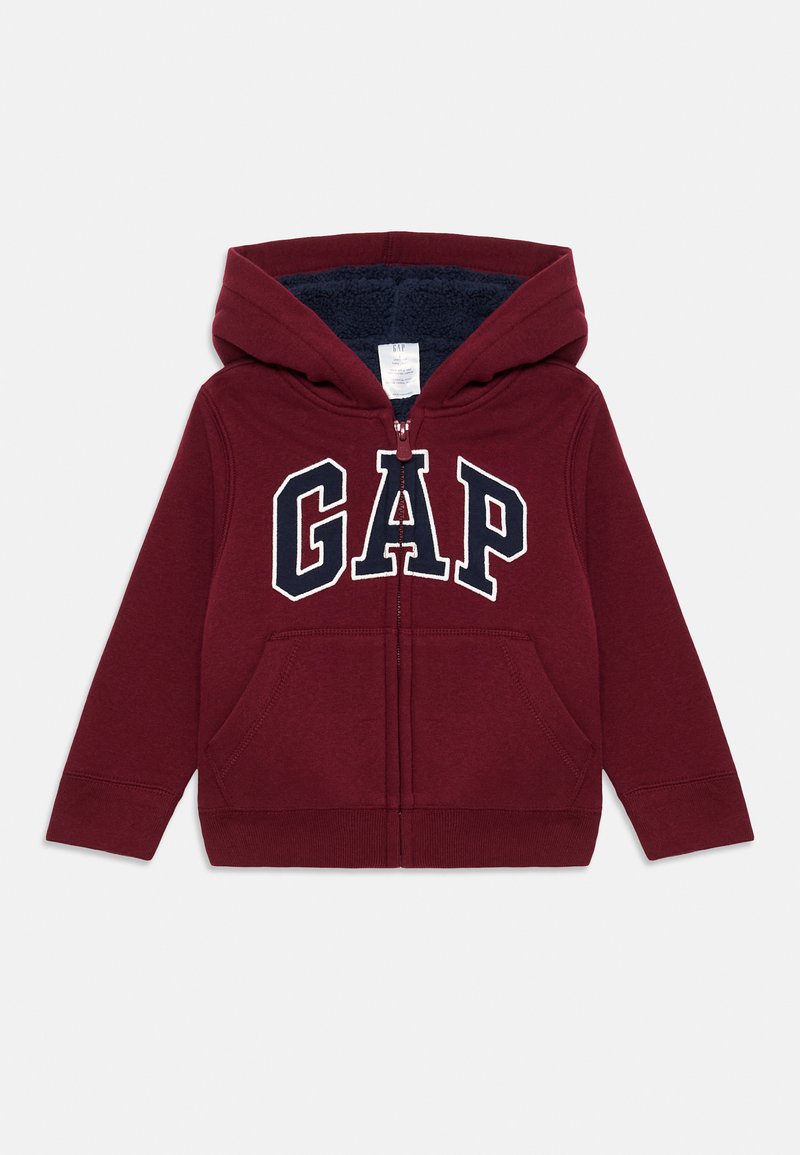 Felpa con zip color bordeaux, con interno in pile, tasche frontali e un grande logo GAP in blu navy sul petto. Presenta polsini e orlo a costine.