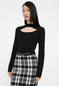 Camisola preta de manga comprida com decote recortado, combinada com saia de cintura alta às riscas em preto e cinzento, com um cinto preto com fivela redonda.