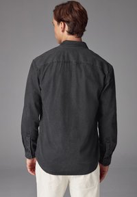 Camicia nera a maniche lunghe con colletto a punta e texture liscia. Presenta dettagli di cucitura e polsini con chiusura a bottoni.