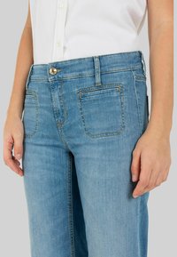 Lichtblauwe denim jeans met een klassiek vijf-pocket ontwerp, voorzien van koperen stiksels en een zilveren knop bij de taille. Soepele textuur.