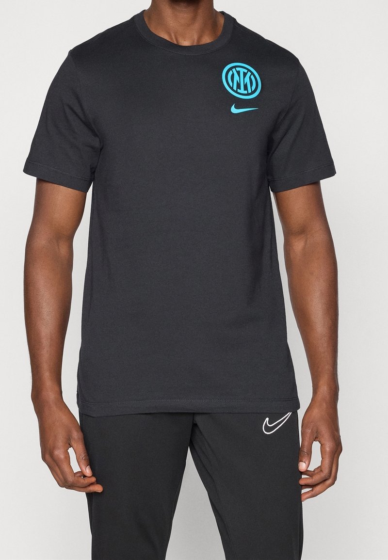 Homme portant un t-shirt noir Nike avec le logo bleu de l’Inter Milan et un pantalon noir avec le logo Nike blanc, debout sur un fond uni.