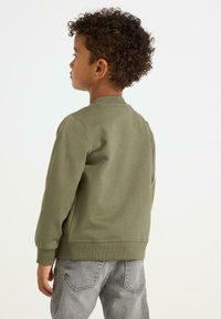 Grüner Sweatshirt mit geripptem Kragen und Bündchen, weicher Textur, getragen mit grauen Jeans, Ansicht von hinten, die die Passform und das Design hervorhebt.
