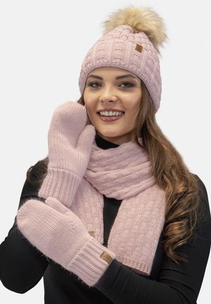 Accessori invernali lavorati a maglia di colore rosa chiaro: un berretto con pompon, una sciarpa coordinata e guanti con polsini a coste e etichette di marca.