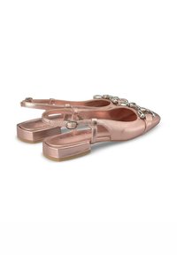 Zapatos slingback en color rosa dorado con puntera puntiaguda, correas metálicas y tacones planos. Presentan un acento decorativo de cadena en la parte frontal.