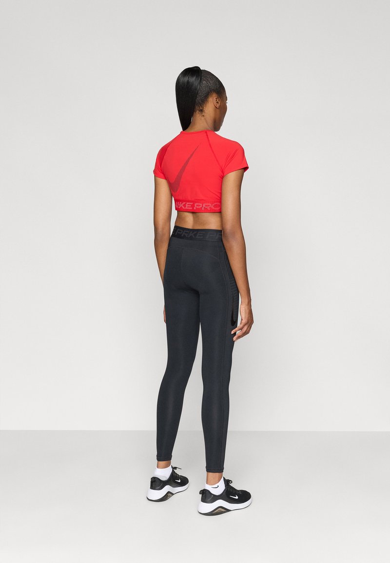 Red cropped athletic top with a logo on the back, paired with black fitted leggings and black sneakers. Flat shoes have white accents.