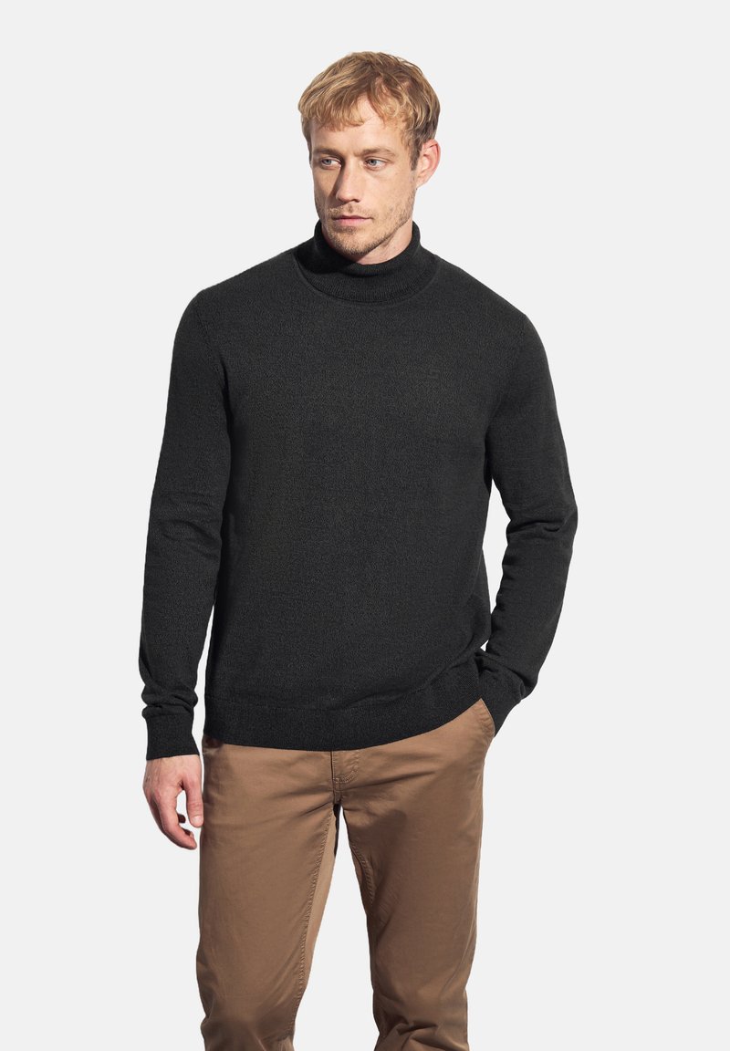 Jersey de cuello alto negro con un acabado texturizado, corte ajustado y puños y dobladillo acanalados, combinado con pantalones marrón claro.