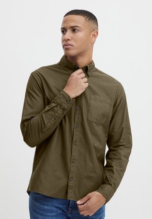 Dark olive green button-up shirt made of soft fabric, featuring a chest pocket, long sleeves, and black buttons. Worn with blue jeans.