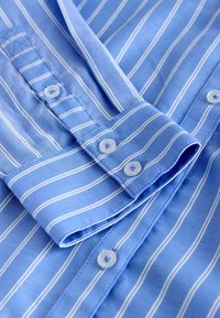 Light blue button-up shirt with white stripes. Made of smooth fabric, features a pointed collar and buttons with small blue accents.