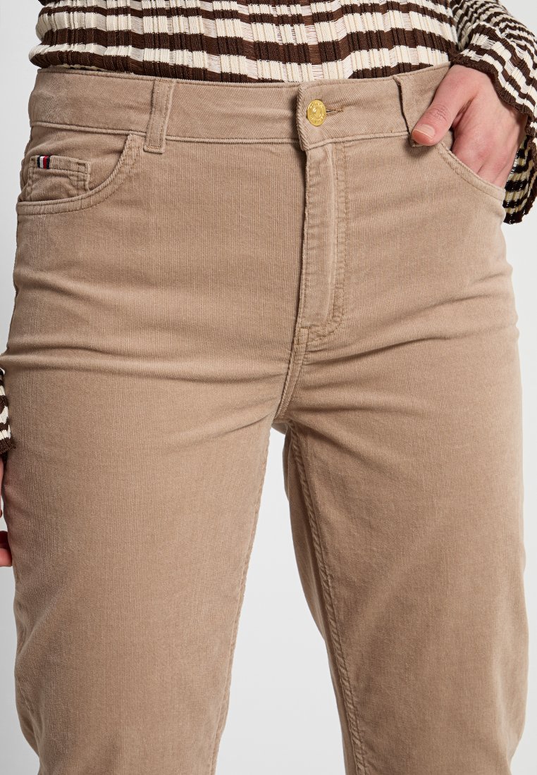 Beige Cordhosen mit geradem Schnitt, ausgestattet mit einer Vordertasche, einem goldenen Knopfverschluss und einer subtilen Textur des Cord-Stoffs.