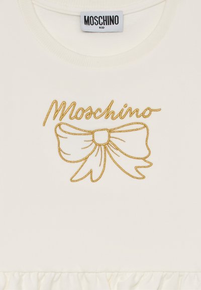 T-shirt bianco con logo "Moschino" ricamato in oro e un grande design a fiocco. Il tessuto ha una consistenza liscia con orlo arricciato.