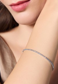 Srebrna bransoletka z przezroczystymi kamieniami szlachetnymi, charakteryzująca się delikatnym, elastycznym wzornictwem, które wygodnie leży na nadgarstku, podkreślająca wysoki połysk.