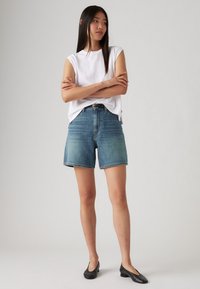 Jeansshorts i en ljusblå tvätt med rak skärning, featuring hög midja och rå kant. Här i kombination med en lösvit ärmlös topp.