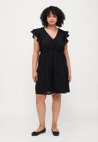Black dress with ruffled sleeves, V-neckline, and textured fabric. Features a fitted waist and tiered skirt. Paired with black flat shoes.