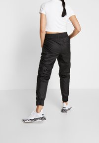 Svarta joggers med elastisk midja och muddade anklar, kombinerade med vita sneakers med svart-vit mönstrad sula.