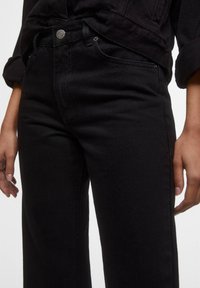 Jeans in denim nero con una vestibilità dritta classica, dotati di tasche anteriori, chiusura con bottone e dettagli di cucitura discreti.