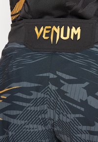Fekete sportnadrág texturált mintával, szürke kiegészítőkkel. Fekete derékpánt arany "VENUM" logóval.
